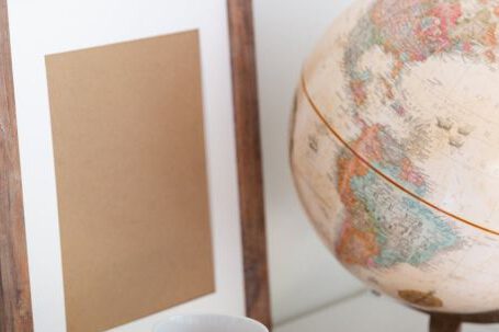 Retro Home - Vintage globe near blank frame and cup of tea placed on book in office