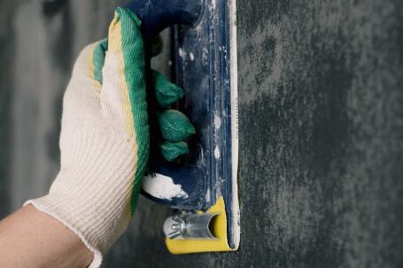 DIY Projects - Crop anonymous male worker in gloves holding scraper and aligning walls in flat