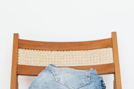 Storage Solutions - Stack of blue jeans of different shades on modern wooden chair against white wall