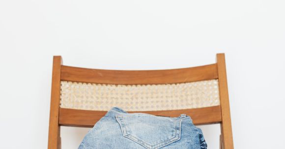 Storage Solutions - Stack of blue jeans of different shades on modern wooden chair against white wall